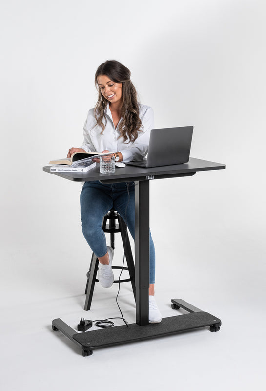 Frau arbeitet auf einem Sitzhocker am Yaasa Desk One mit Schreibtisch-Rollen