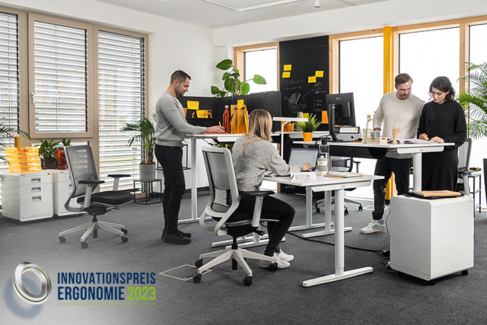Vier Personen arbeiten im Sitzen und Stehen mit ergonomischen Büromöbeln