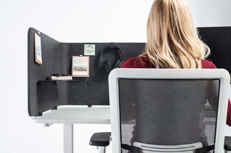 Frau arbeitet im Sitzen auf einem Schreibtisch mit einer Tischtrennwand um die Ecke montiert