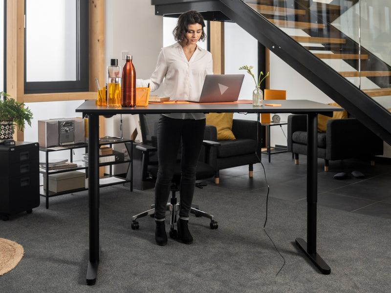 Frau arbeitet im Stehen an einem höhenverstellbaren Schreibtisch und genießt die Vorteile