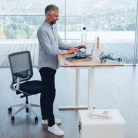 Mann arbeitet im Stehen am Yaasa Desk Pro 2 in Vollholz Eiche/Weiss