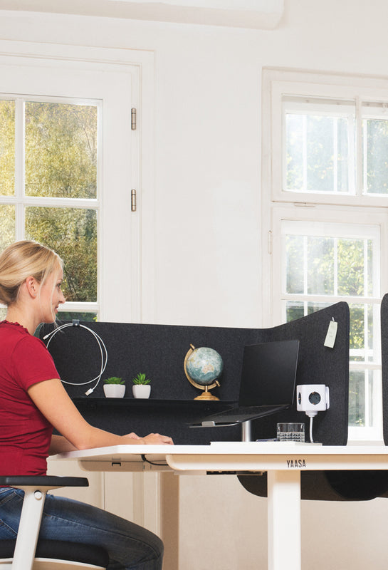 Frau arbeitet im Sitzen an einem Schreibtisch mit der Yaasa Privacy Wall ums Eck montiert