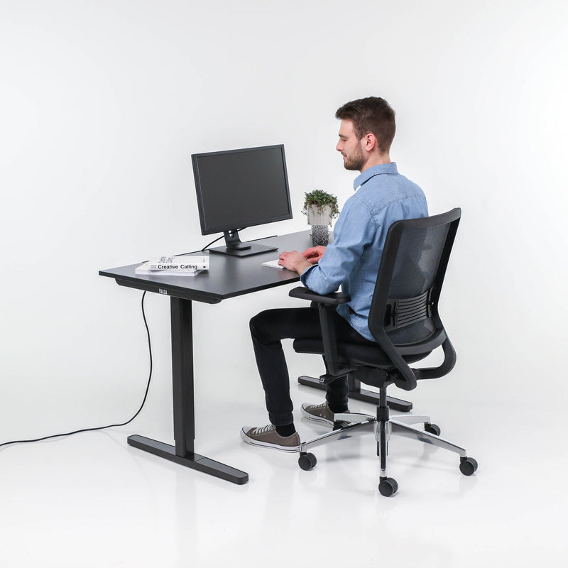 Mann sitzt auf dem schwarzen Yaasa Chair und arbeitet am höhenverstellbaren Tisch Desk Basic.